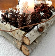 some pine cones and candles are in a wooden tray on a bed with white sheets