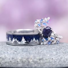 two wedding rings with blue and white diamonds on them sitting on top of a rock