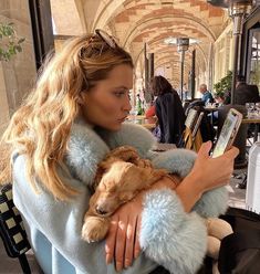 a woman holding a dog in her arms while sitting on a bench at an outdoor cafe