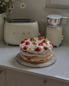 a cake sitting on top of a kitchen counter next to toaster ovens and flowers