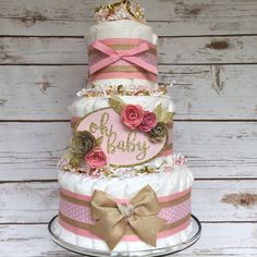 a three tiered cake decorated with pink, gold and white ribbons on a platter