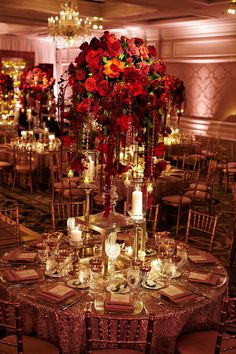 a table with many candles and flowers on it in a room filled with tall centerpieces