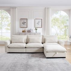 a large white sectional couch in a living room with two windows and a rug on the floor