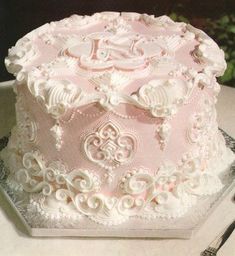 a pink and white decorated cake sitting on top of a table next to silverware