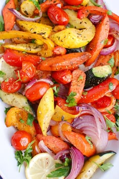 a white plate topped with lots of different types of veggies and lemon wedges