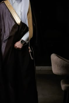 a man in a robe and tie standing next to a chair