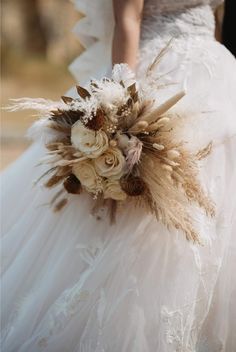 a woman in a wedding dress holding a bouquet with dried flowers and feathers on it