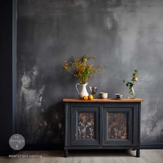 two vases with flowers and fruit on top of a table in front of a gray wall