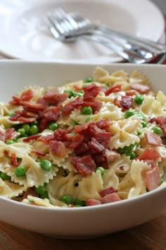 a bowl filled with pasta and peas on top of a wooden table next to silverware