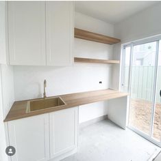 an empty kitchen with white cabinets and wood counter tops, in front of a sliding glass door