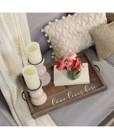 a tray with candles and flowers on it sitting on a couch next to a pillow