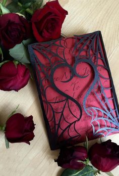 red roses are sitting next to a black and pink card holder with a heart on it