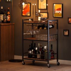 a bar cart with bottles and glasses on it in front of a wall full of pictures