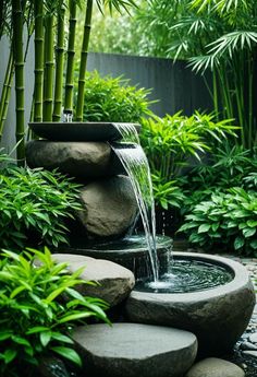 a water fountain surrounded by rocks and bamboo trees in a garden area with green plants