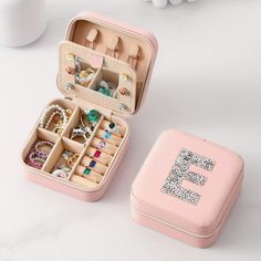 an open pink jewelry box sitting on top of a white table next to a cup