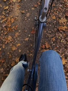 the legs of a person riding a bike on a path with leaves all over it