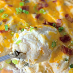 a spoon full of mashed potatoes with bacon, green onions and cheese on top