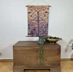 a painting hanging on the wall next to a wooden chest with a plant growing out of it