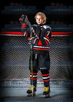 a young boy in hockey uniform standing next to the net with his hands up and holding a hockey stick