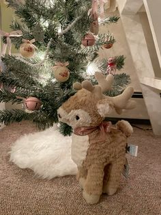 a stuffed deer sitting next to a christmas tree in front of a staircase case with ornaments on it