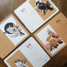 four calendars with birds and flowers on them sitting on top of a wooden table