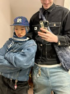 a man standing next to a little boy wearing a jacket and hat while holding a cell phone