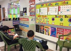 two young boys sitting in green chairs at desks with computers and posters on the wall behind them