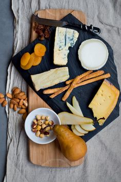 an assortment of cheeses, nuts and crackers on a black platter with a knife