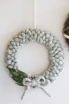 a knitted wreath hanging on the wall next to a bird's nest with a green leaf