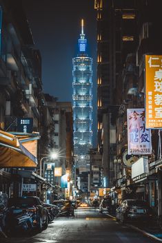 a city street at night with tall buildings in the background