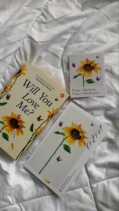 two books laying on top of a bed next to each other, one with a sunflower