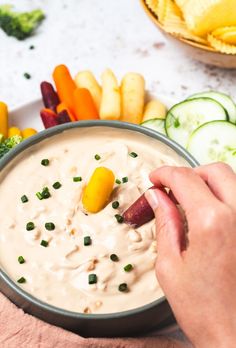 a person dipping something into a bowl of dip surrounded by veggies and crackers