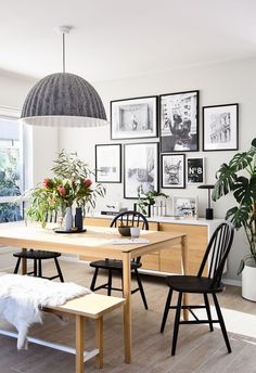 a dining room table with chairs and pictures on the wall above it, next to a bench