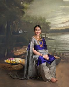 a woman sitting in front of a painting wearing a blue and silver sari with her hands on her hips