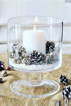 a candle in a glass bowl filled with snow and pine cones