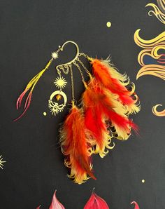 two feathers are hanging from a chain on a black surface with gold and red designs