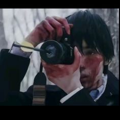 a man holding a camera up to his face with blood all over it's body