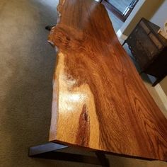 a large wooden table with metal legs on carpeted floor next to wall and window