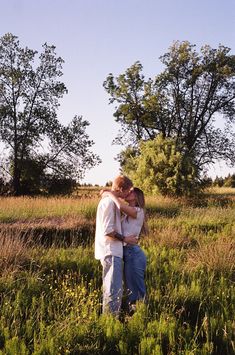 two people standing in the middle of a field with trees behind them and one person hugging his head