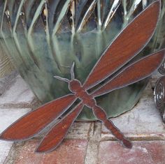 a metal dragonfly sitting on top of a potted plant next to a brick walkway