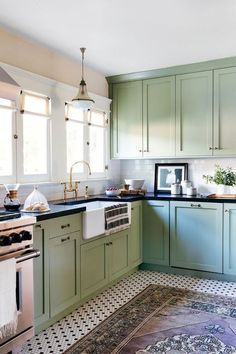 a kitchen with green cabinets and black counter tops, an area rug on the floor