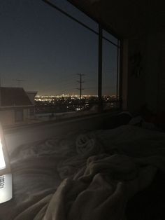 a laptop computer sitting on top of a bed under a window at night with city lights in the background