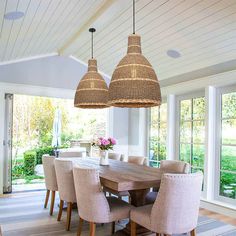 a dining room table with chairs and lights hanging from it's ceiling in front of large windows