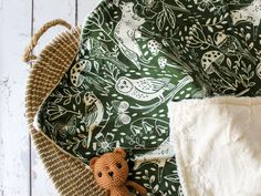 a brown teddy bear sitting on top of a green and white blanket next to a wicker basket