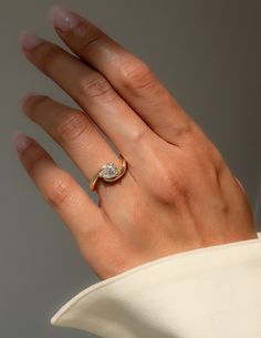 a woman's hand wearing a gold ring with a white diamond on the middle