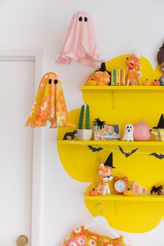 halloween decorations are displayed on yellow shelves in the corner of a room with white walls