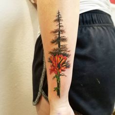 a woman's arm with a pine tree and flower tattoo on the left forearm