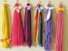 four different colored tassels hanging on a wall with bows and ribbons attached to them