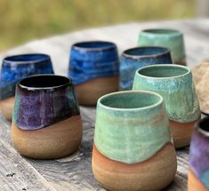 there are many different colored cups sitting on the wooden table with one cup in the middle