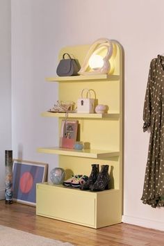 a yellow shelf with shoes and purses on it next to a wall mounted coat rack